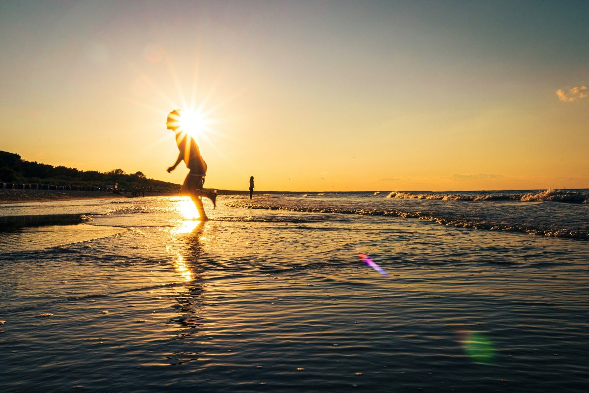 Kind läuft bei Sonnenuntergang durch das flache Wasser der Ostsee