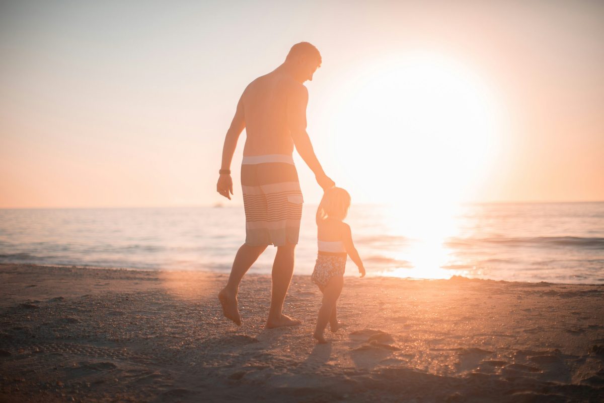 Silhouette eines Vaters und seines Kindes, Hand in Hand am Strand beim Sonnenuntergang.