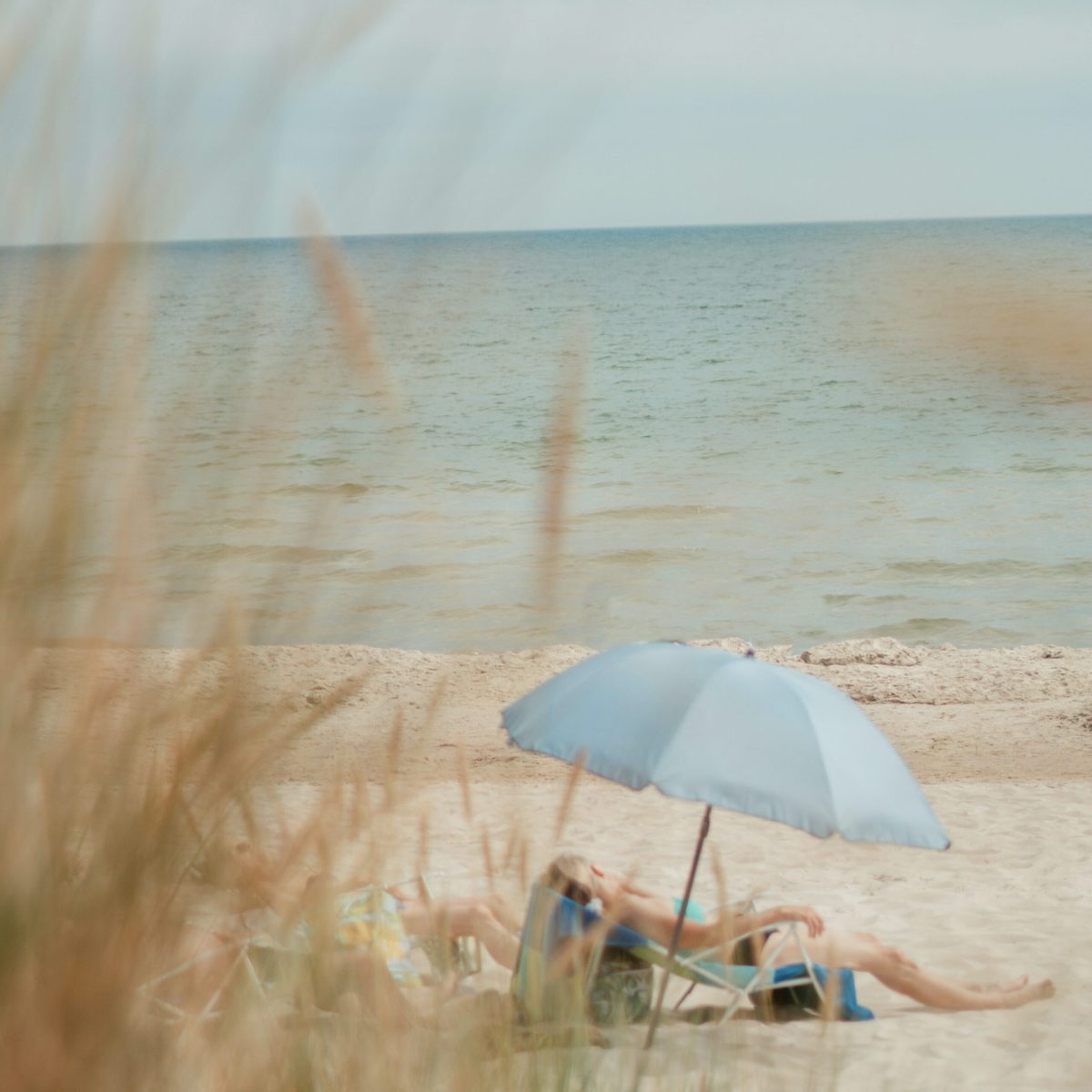 Ruhiger Strandtag mit blauem Sonnenschirm und entspannenden Personen am Meer