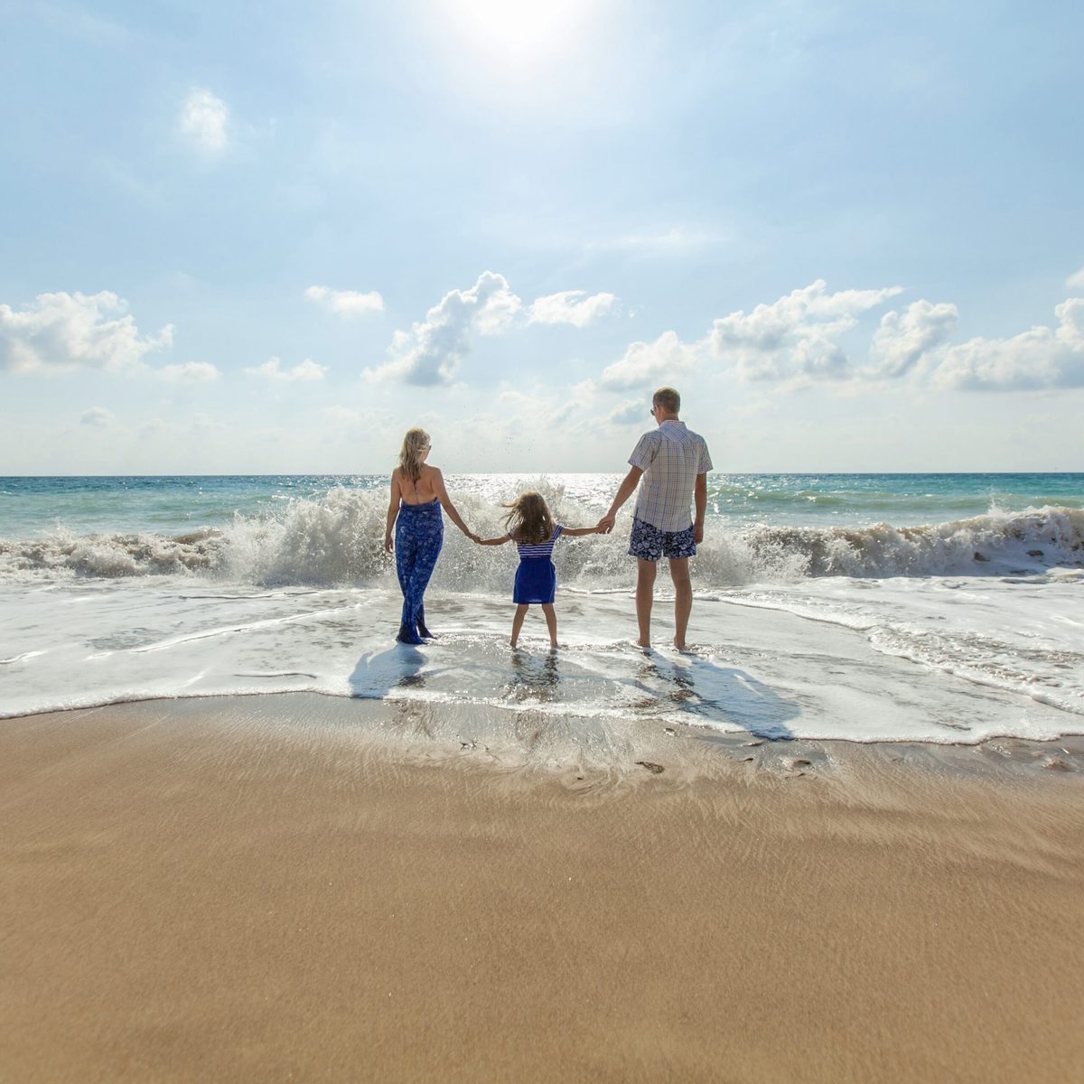 Familie mit Kind steht Hand in Hand am Ostseestrand und blickt auf die ankommenden Wellen