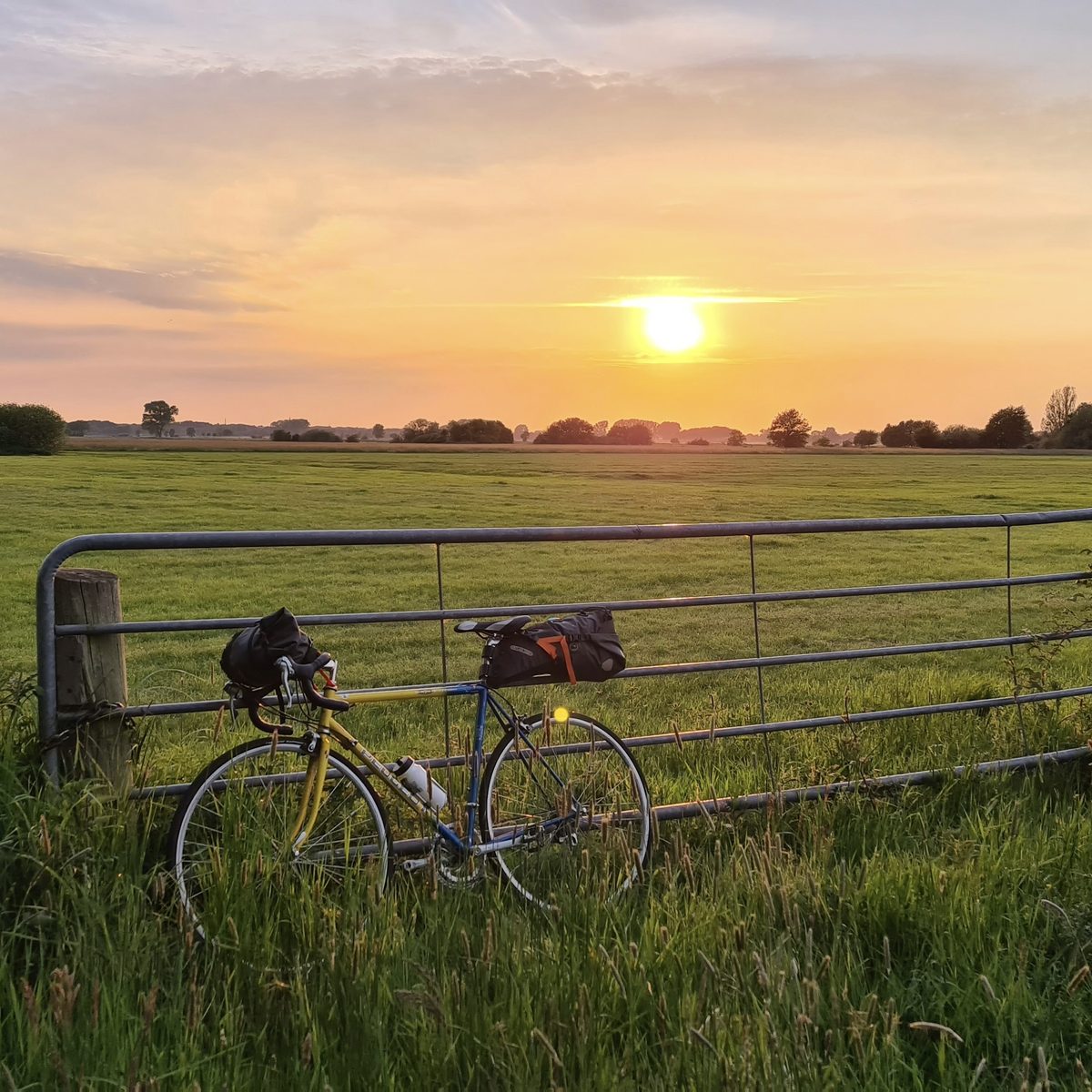 Fahrrad lehnt an einem Zaun mit Blick auf das Feld bei Sonnenuntergang an der Ostsee