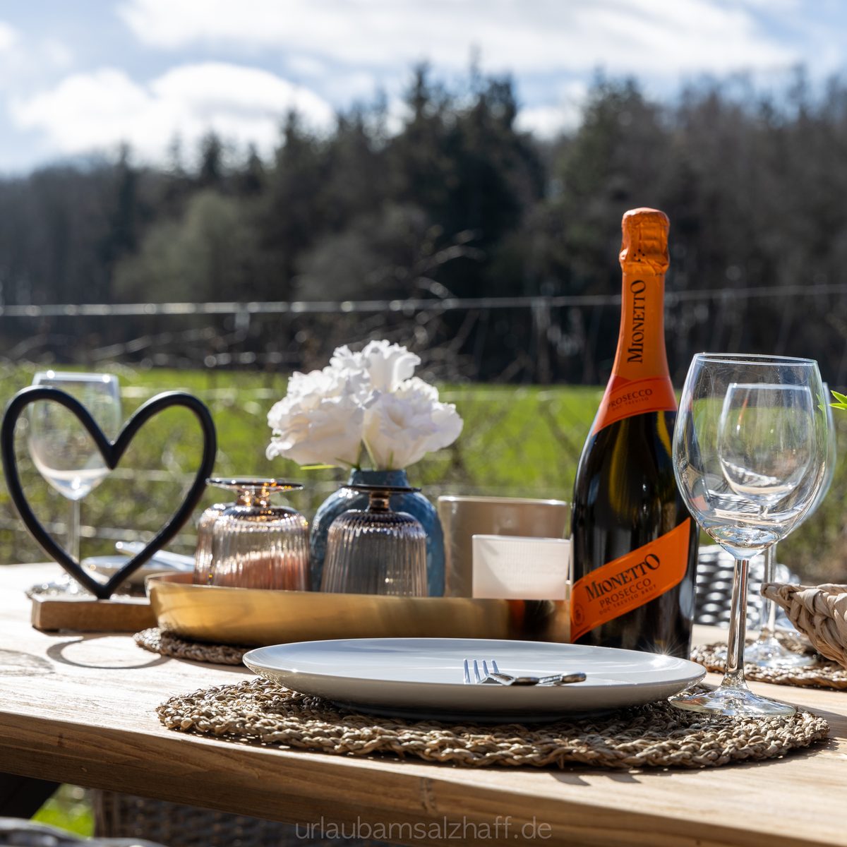 Idyllisch gedeckter Tisch im Freien mit Prosecco und Ausblick auf die Natur.