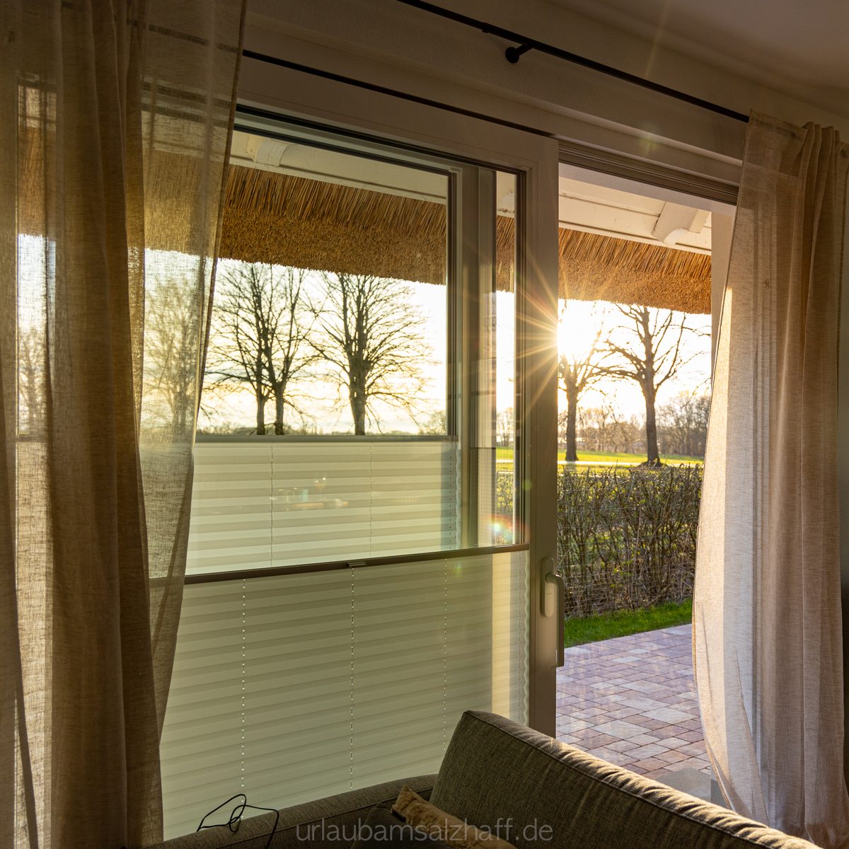Blick aus dem Fenster auf ein Sonnenuntergangspanorama zwischen Bäumen.