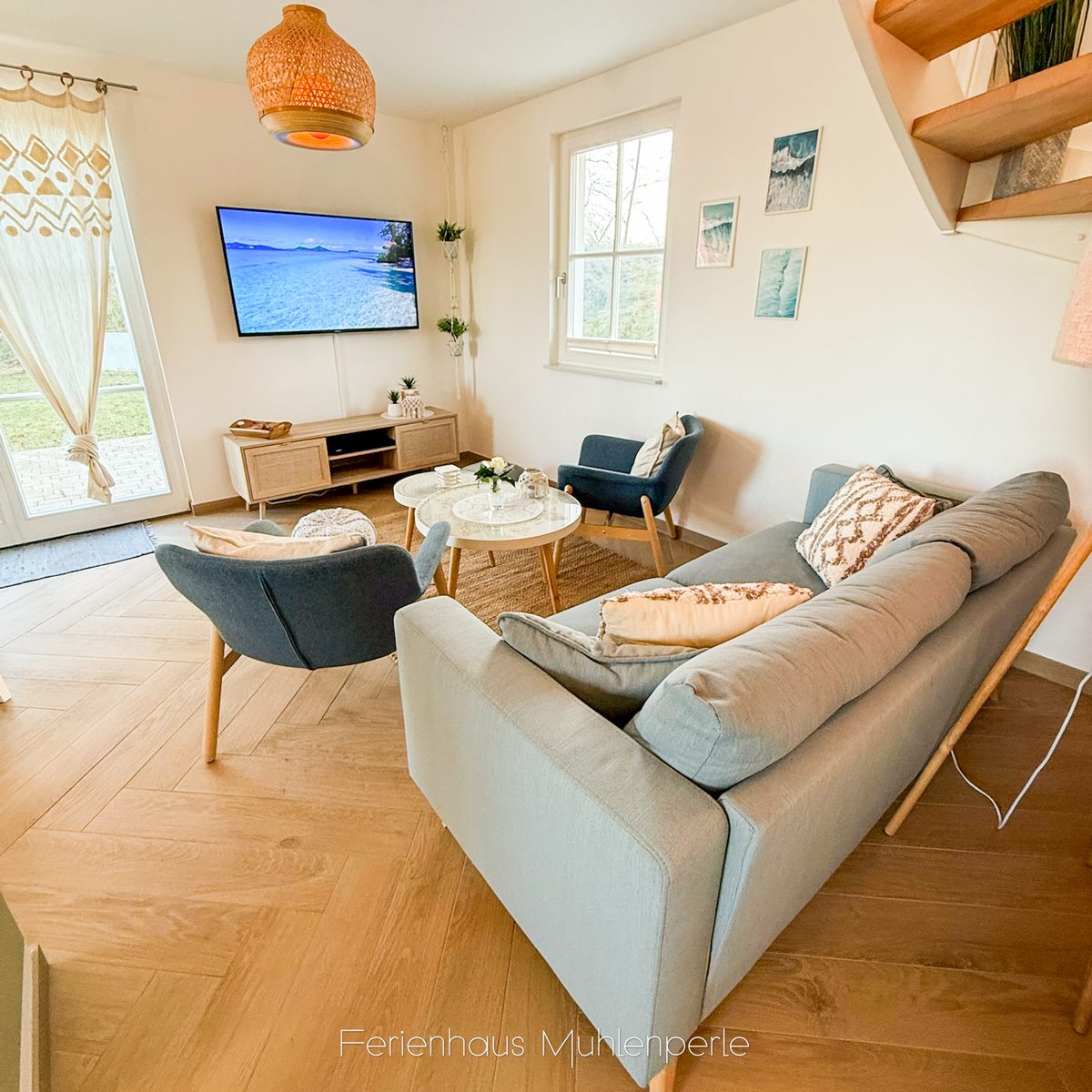 Gemütlicher Wohnbereich im Ferienhaus Mühlenperle mit Sofa, Sesseln, Smart-TV und Blick auf die