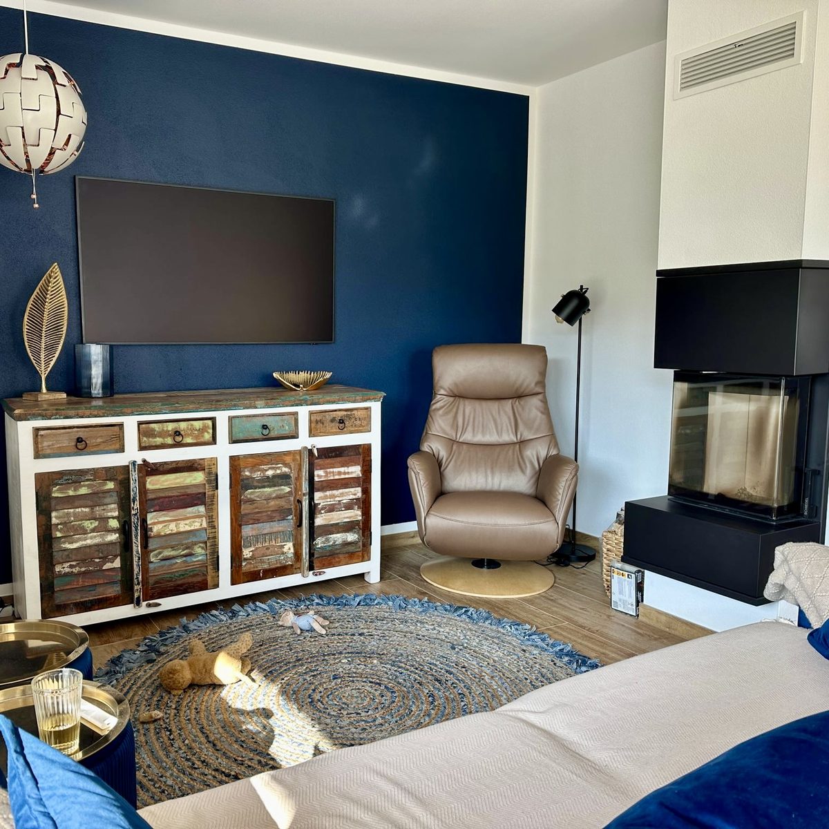 Wohnzimmer mit dunkelblauer Wand, bequemem Sessel und modernem Kamin.