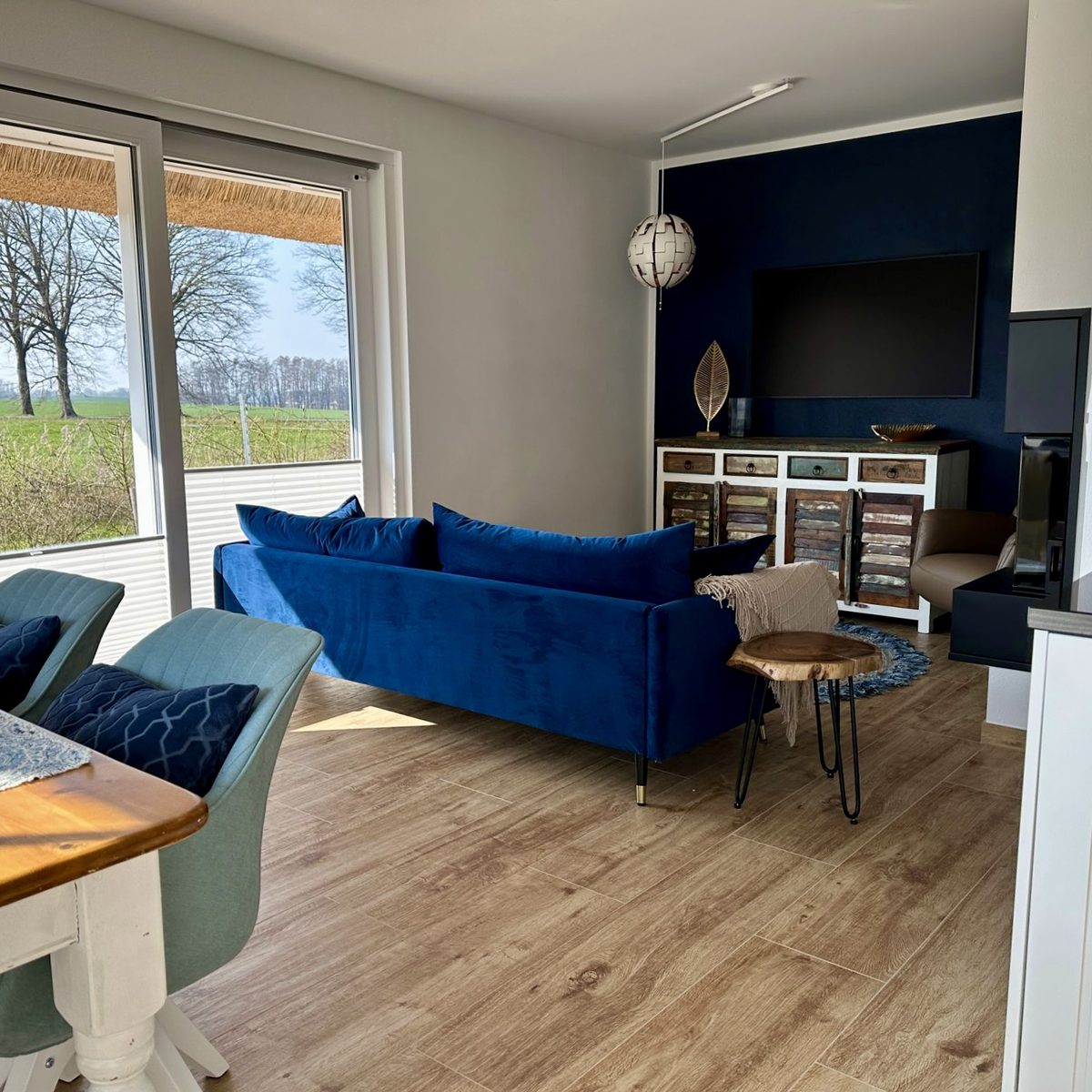 Blick von der Küche auf ein einladendes Wohnzimmer mit blauem Sofa und Blick ins Grüne.