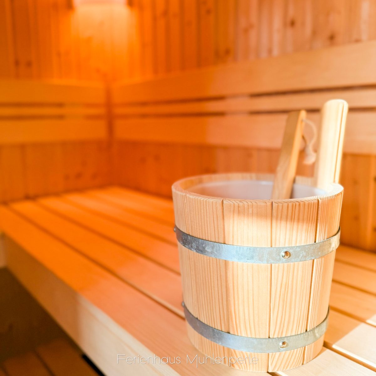 Innenansicht der Sauna im Ferienhaus Mühlenperle mit einem hölzernen Aufgusskübel und Schöpfkel