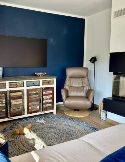 Wohnzimmer mit dunkelblauer Wand, bequemem Sessel und modernem Kamin.
