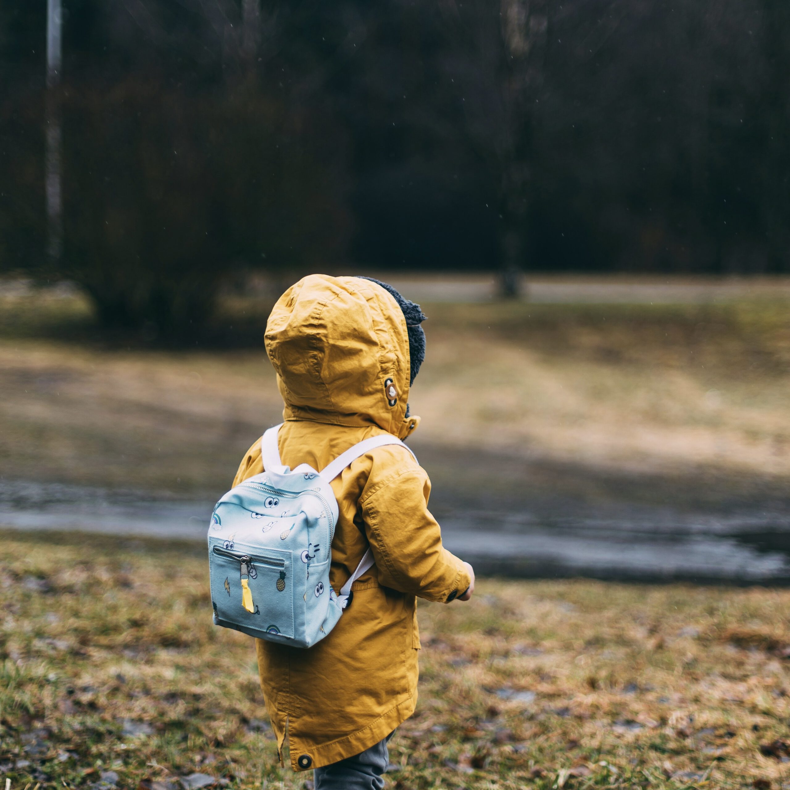 Kind mit gelber Regenjacke und Rucksack auf einem Wanderweg in der Natur