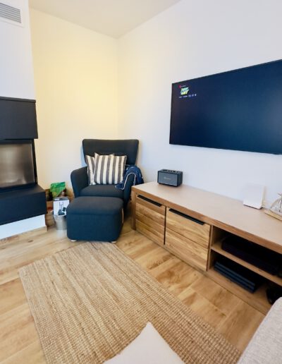 Wohnzimmer mit Kamin im Ferienhaus KiteZeit, gemütlich eingerichtet mit Sofa und TV.