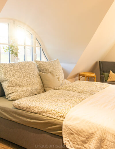 Weites, einladendes Doppelbett in einem lichtdurchfluteten Schlafzimmer mit stilvoller Sitzgelegenheit.