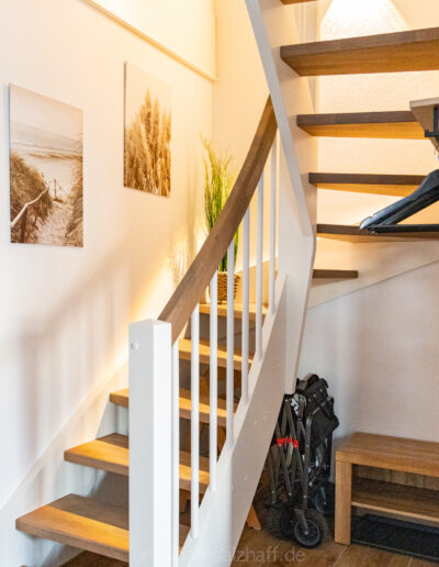 Helles Treppenhaus mit elegantem Geländer und stimmungsvollen Bildern der Küstenlandschaft.